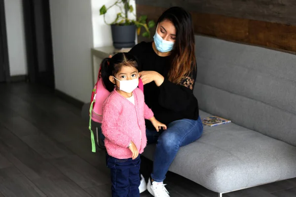 latin mom and 3 year old girl with protective face masks and backpack for back to school, new normal covid-19