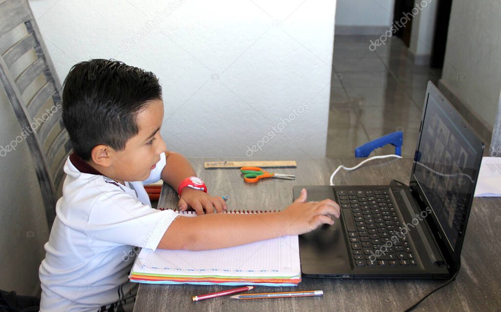 back to school, 7 year old Latino boy in online home classes with laptop and school supplies