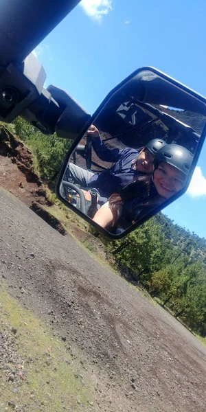 Latin adult couple, view from a buggy car capable of driving on difficult terrain, such as dirt and mud, you can see the rear-view mirror and the road that leads to adventure