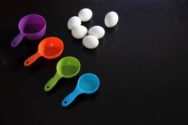 Ölçmek için mutfak gereçleri ve siyah masa arkasında yumurtalar