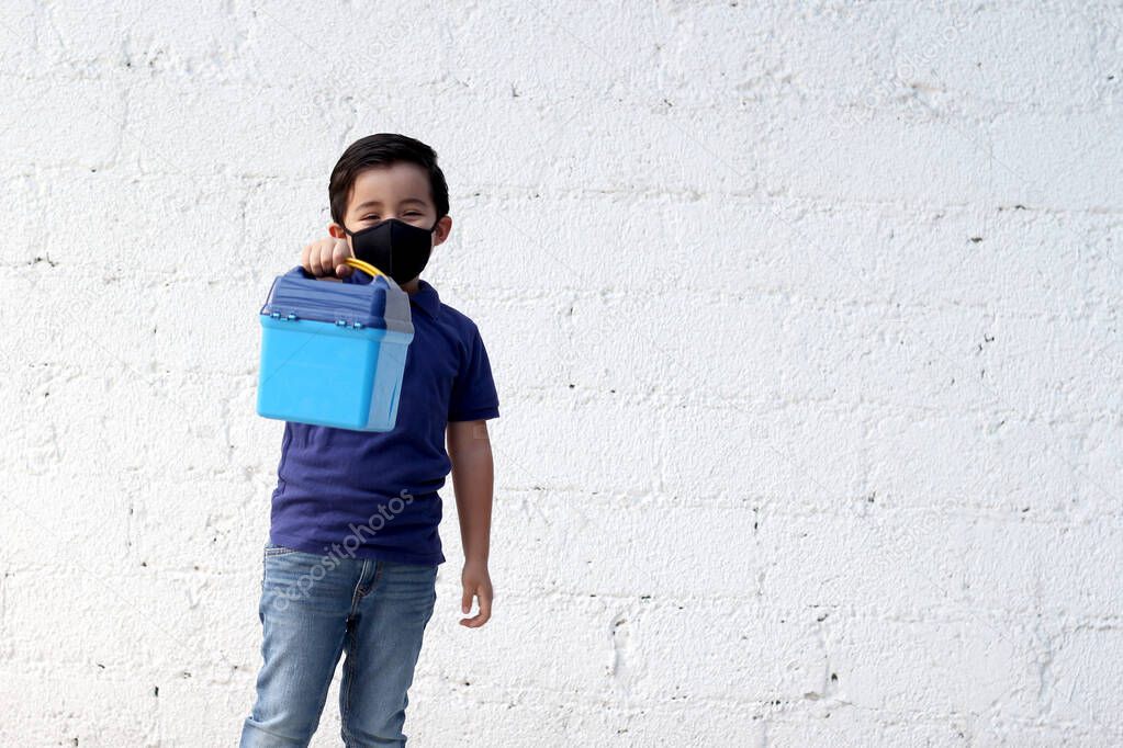 6-year-old boy with protective mask, lunch box and colors for back to school, new normal covid-19