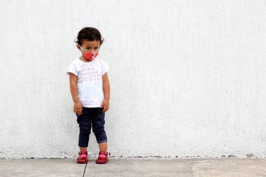 Beyaz duvar arka planında koruyucu maskesi olan 2 yaşında Latin bir kız.