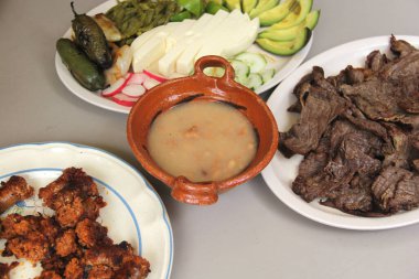 Tipik Meksika yemeği, kızarmış biftek ve peynirli sosis nopales, kırmızı biber, avokado ve fasulyeli kil tabağı.