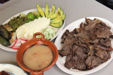 Tipik Meksika yemeği, kızarmış biftek ve peynirli sosis nopales, kırmızı biber, avokado ve fasulyeli kil tabağı.