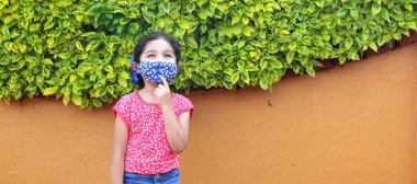 6 yaşındaki Latin kız covid-19 koruyucu maskeli, arka planda bitki örtüsü olan, yeni normal