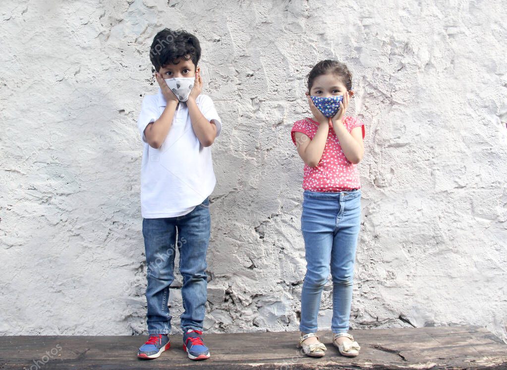6-year-old Latino children with covid-19 face masks, sitting with a white wall in the background,new normal