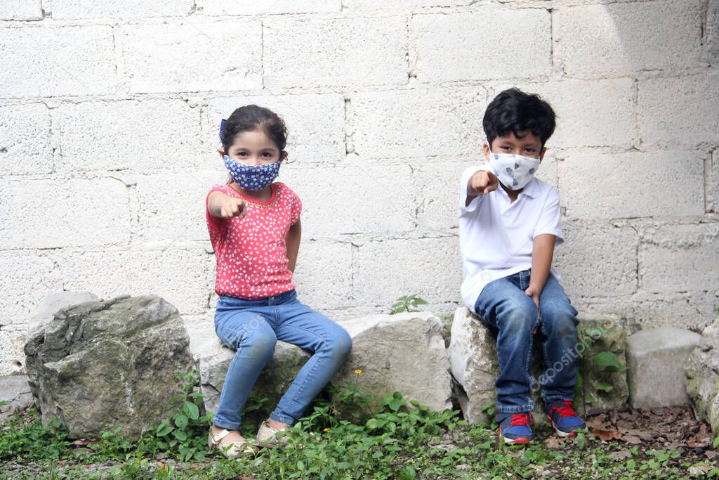 6-year-old Latino children with covid-19 face masks, sitting with a white wall in the background,new normal