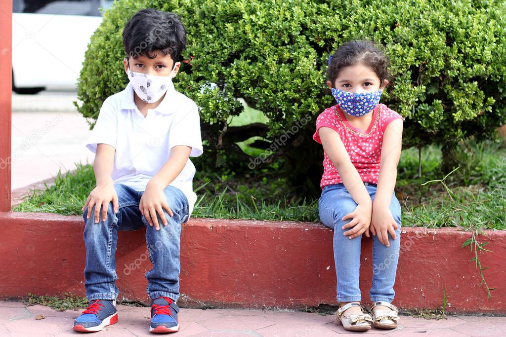 6-year-old boy and girl with protective masks for the covid-19 virus, sitting in the park, new normal