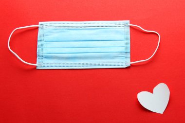 Klinik kullanım için üç katmanlı koruyucu maske ve kırmızı arka planda beyaz kalpler.