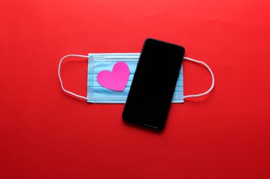 Covid-19 'dan Sevgililer Günü salgını koruyucu maskeli cep telefonu klinik kullanım ve pembe kalpler.