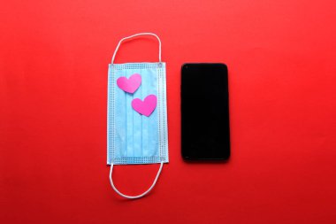Covid-19 'dan Sevgililer Günü salgını koruyucu maskeli cep telefonu klinik kullanım ve pembe kalpler.