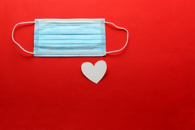 Klinik kullanım için üç katmanlı koruyucu maske ve kırmızı arka planda beyaz kalpler.