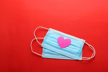 Klinik kullanım için üç katmanlı koruma maskesi ve kırmızı arka planda pembe kalpler.