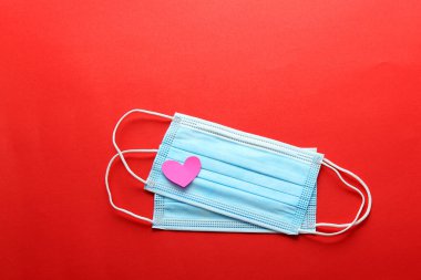 Klinik kullanım için üç katmanlı koruma maskesi ve kırmızı arka planda pembe kalpler.