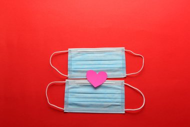 Klinik kullanım için üç katmanlı koruma maskesi ve kırmızı arka planda pembe kalpler.