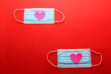 Klinik kullanım için üç katmanlı koruma maskesi ve kırmızı arka planda pembe kalpler.