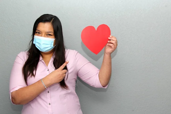 latin woman with protection mask clinical use and red heart, valentine in contingency covid-19