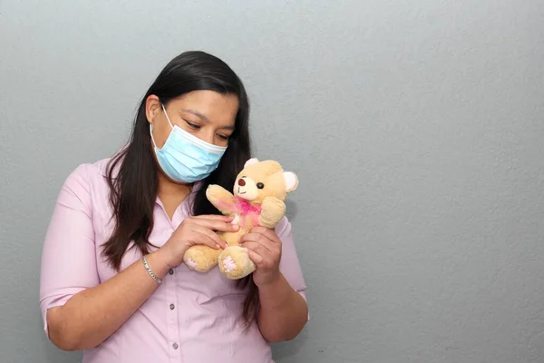 latin woman with protection mask clinical use and valentine gifts in contingency covid-19, teddy bear, blackboard and heart