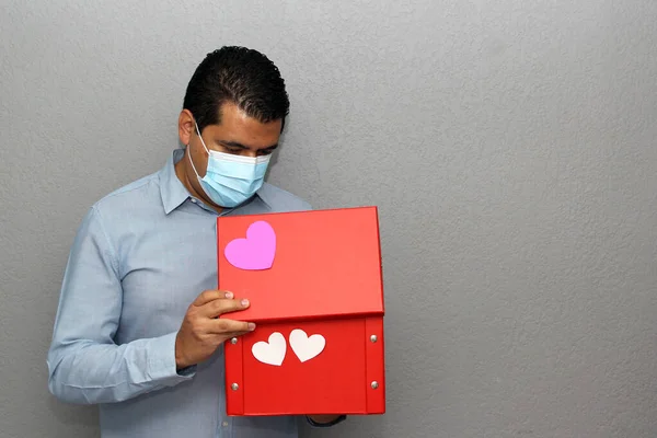 Valentine\'s Day. latin man with protection mask and red gift box with white hearts in covid-19 pandemic