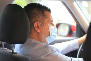 Latin adam şoförü, araç içinde koruma maskesi takıyor.