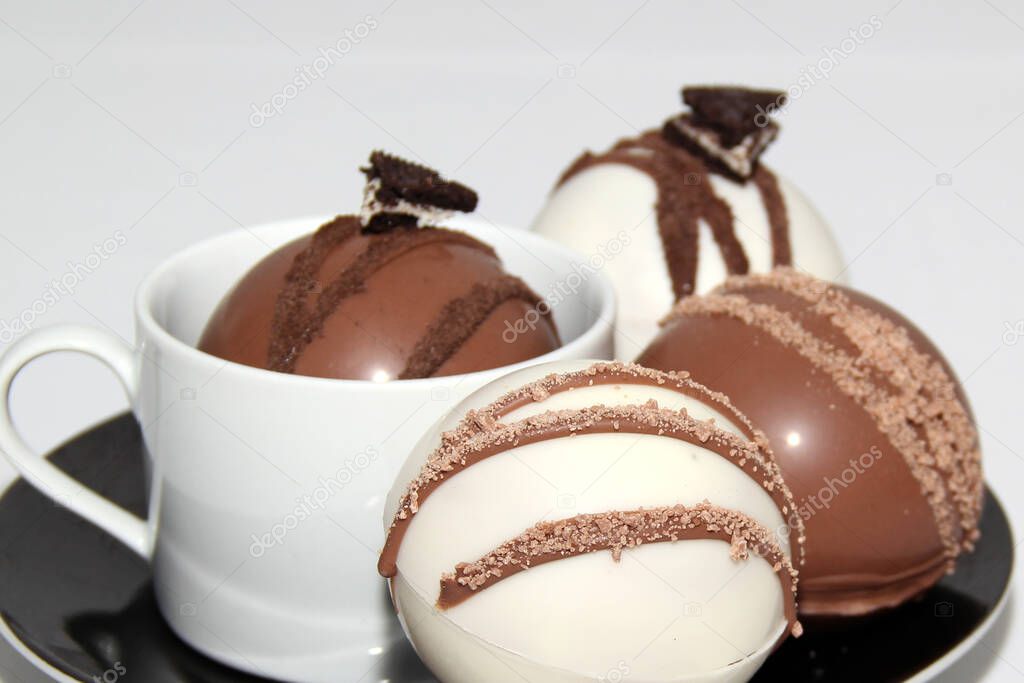 chocolate bombs in mug with hot milk, filled with marshmallows and white chocolate on white background