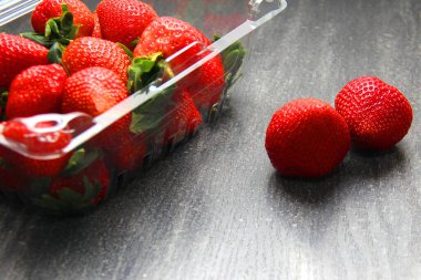 Plastik ambalajda meyve, kırmızı çilek. Klasik gri ahşap arkaplan