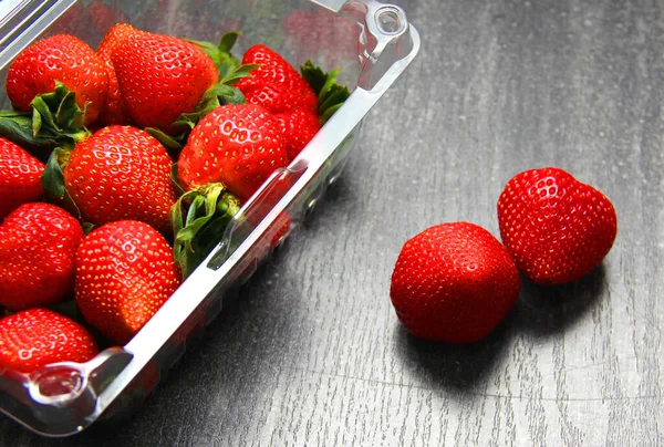 Plastik ambalajda meyve, kırmızı çilek. Klasik gri ahşap arkaplan