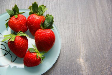 Beyaz tabakta kırmızı meyveli çilek. Klasik gri ahşap arkaplan