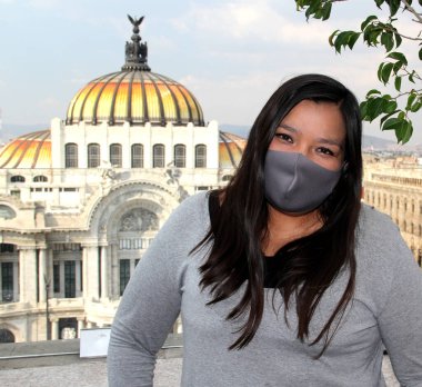 Meksika 'da koruma maskeli Latin bir kadın. Arka planda normal ve tarihi anıtlar var. Güzel sanatlar sarayı.