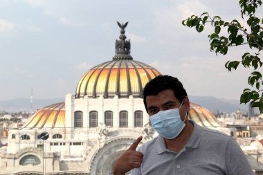 Meksika 'da koruma maskeli Latin bir adam. Arka planda yeni normal ve tarihi anıtlar var. Güzel sanatlar sarayı.