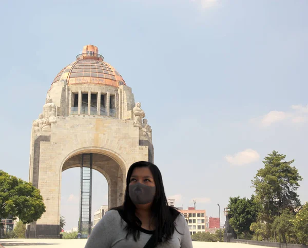 latin woman with protection mask in mexico city with the new normal and the monument of the revolution in the background