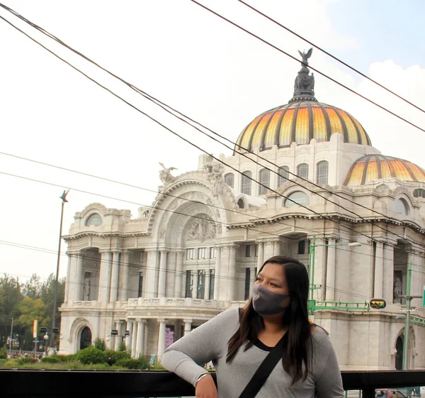 black hair latin woman with protection mask on the street with the new normal by covid-19 and palace of fine arts in mexico city