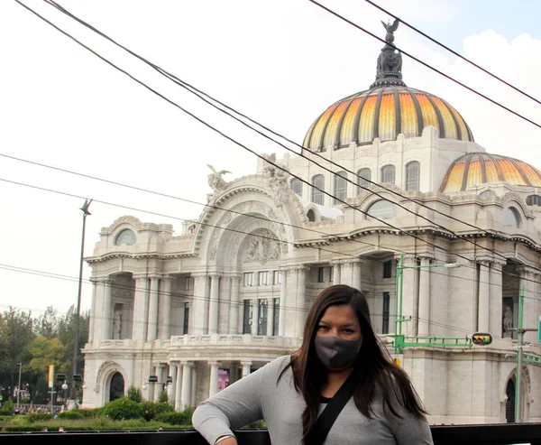 black hair latin woman with protection mask on the street with the new normal by covid-19 and palace of fine arts in mexico city