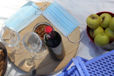 Yakın çekim ve salgın piknik manzarası. Klinik kullanım için şarap, yemek, meyve, tohum ve koruyucu maskeli sepet