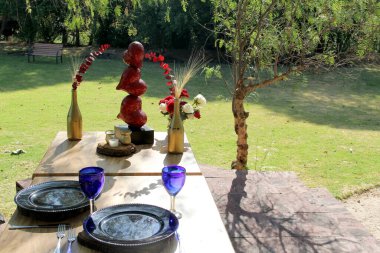 Sevgililer gününde yeşillik, çiçek ve kalp süslemeleriyle romantik yemek takımı ve mavi bardaklar.