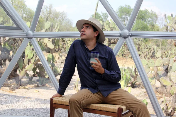 latin man tourist with hat inside glamping room in mexico desert and drinking lemonade