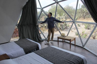 Jeodezik bir çadırın içinde gökyüzünü ve yıldızları görmek için saydam çatısı olan Latin bir adam.