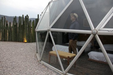 Latin bir adam jeodezik bir çadırın penceresinden manzaranın keyfini çıkarıyor.