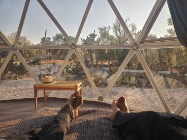 Çift yatağında uzanmış güneşin doğuşunu jeodezik çadır penceresinden izliyor.