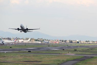 Uçak pistten kalkıyor, bulutların arasında uçuyor, yüksekliğini arttırıyor.