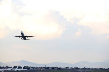 Mavi gökyüzü ile büyük bulutlar arasında uçak kalkıyor.