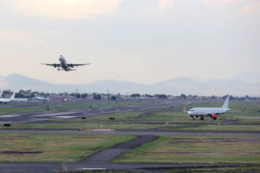 Mavi gökyüzü ile büyük bulutlar arasında uçak kalkıyor.