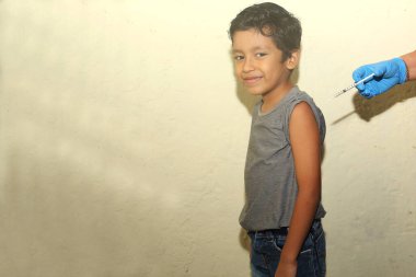 7 yaşındaki Latin çocuk koluna aşı aşısı vuruluyor. Mutlu ve korkmuş.