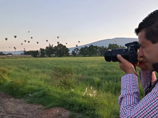 空を飛ぶカラフルな熱気球の写真を撮るカメラやレンズを持つプロの写真家 — ストック写真