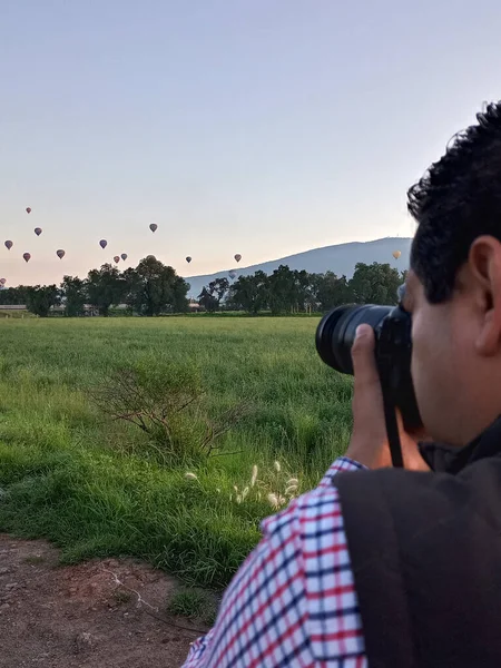 空を飛ぶカラフルな熱気球の写真を撮るカメラやレンズを持つプロの写真家 — ストック写真