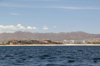 Palmiye ağaçları, arka planda dağlar ve muhteşem manzaralarla dolu tatillerin tadını çıkaran insanların gölgeleriyle sahili görmek.