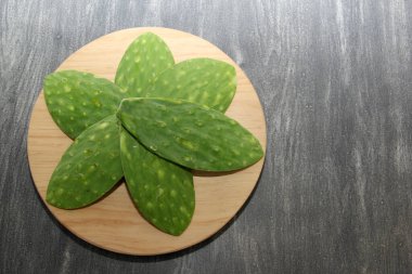 Fresh green nopales without bones on a round wooden chopping board ready to be cooked clipart