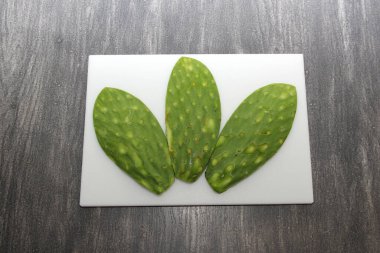 Taze yeşil Meksikalı göçebeler, gri ahşap bir masanın üzerinde beyaz bir kesim tahtasının üzerinde pişirmeye hazırlar.