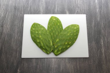 Taze yeşil Meksikalı göçebeler, gri ahşap bir masanın üzerinde beyaz bir kesim tahtasının üzerinde pişirmeye hazırlar.