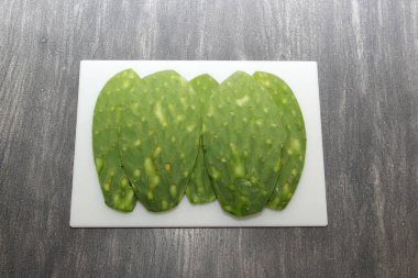 Taze yeşil Meksikalı göçebeler, gri ahşap bir masanın üzerinde beyaz bir kesim tahtasının üzerinde pişirmeye hazırlar.